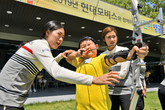 컴파운드 국가대표 소채원(왼쪽부터) 선수와 심예지 선수가 초등학생에게 활 쏘는 법을 알려주고 있다. <현대모비스 제공>